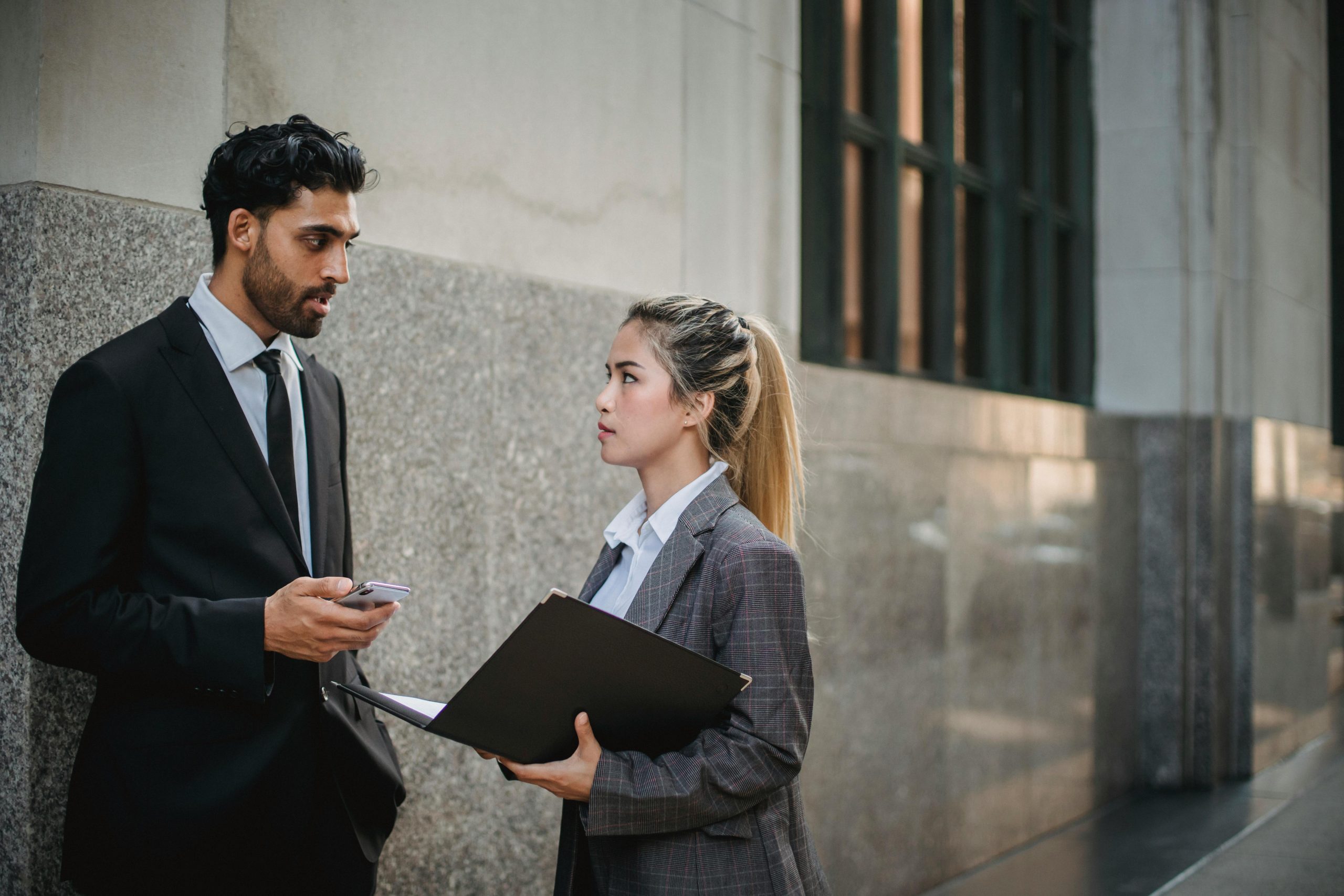 Two professionals in business attire discussing work outside an office building.